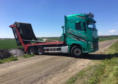 Lastväxlare tömmer container bredvid grusväg